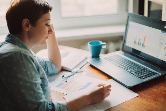 A woman reviewing charts and graphs on paper and on her computer.