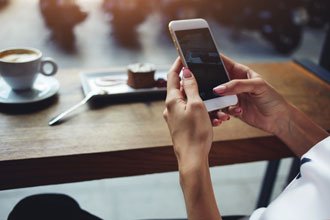 Woman sitting in coffee shop texting on cell phone.